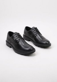 Une paire de chaussures habillées en cuir noir à lacets avec des semelles en caoutchouc robustes sur un fond blanc uni.