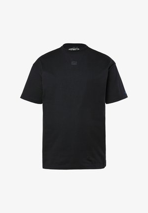 Musta lyhythihainen pyöreäkauluksinen t-paita, jossa pieni keskitetty logo rinnassa ja hillitty brändäys vasemmassa hihassa.