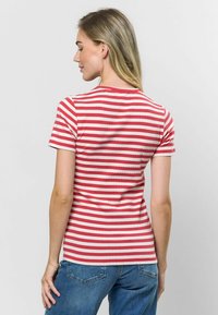 Sarkans un balts svītrains īsās piedurknes T-krekls ar ribotu struktūru, apaļu apkakli un pieguļošu dizainu, apvienots ar zilām džinsu biksēm.