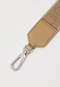 Sangle en tissu beige avec accent en cuir texturé, dotée d'un clip en métal argenté à l'extrémité. Détails cousus visibles.