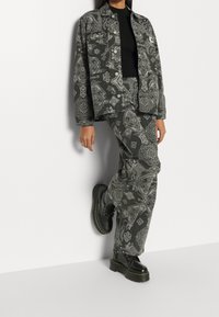 Šedý vzorovaný set obsahující volnější košili a odpovídající kalhoty. Černé masivní boty doplňují celý outfit.