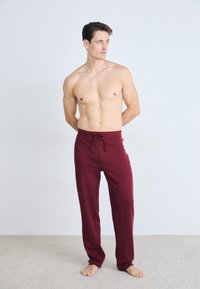 Bordeaux loungebroek met een tailleband met trekkoord, gemaakt van zachte stof, heeft een comfortabele pasvorm en een strak ontwerp zonder patronen of logo's.