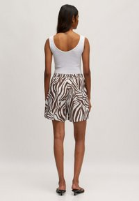 Witte tanktop en bruine shorts met zebra-print en elastische tailleband. Soepele stof; aansluitend bovenstuk, relaxed fit shorts en platte sandalen.