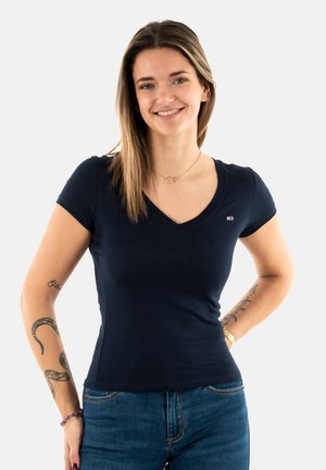 Tamno plava majica s kratkim rukavima i V-izrezom, slim fit, izrađena od mekanog pamuka. Ima mali logo na lijevoj strani grudi. Uparen s trapericama.