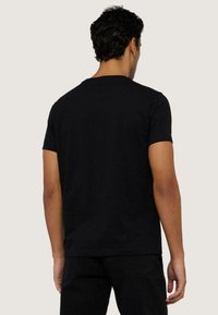 Czarny bawełniany t-shirt z okrągłym dekoltem, krótkimi rękawami i luźnym fasonem. Tył jest gładki, bez widocznych logotypów czy wzorów.