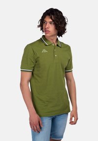 Polo verde con colletto classico, maniche corte e dettagli a righe a contrasto. Presenta un logo sull'area sinistra del petto.