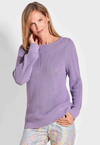Lavendel gebreide trui met een ronde halslijn, geribde manchetten en decoratieve opengehaakte details. Gecombineerd met gemusterde pastelkleurige broek.