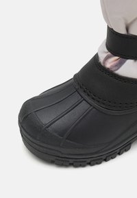 Bota de goma negra con puntera texturizada, correa ajustable y sección superior de textil con diseño. Presenta un diseño estampado cerca del caña.