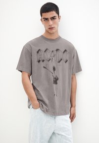 Tricou din bumbac gri, cu logo-ul AC/DC și un design grafic al unui chitarist. Mâneci scurte și croială relaxată. Asortat cu blugi ușor decolorati, de culoare albastru deschis.