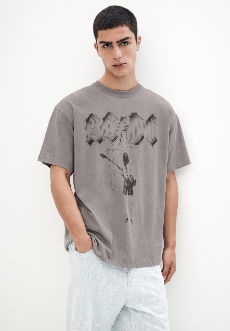 Tricou din bumbac gri, cu logo-ul AC/DC și un design grafic al unui chitarist. Mâneci scurte și croială relaxată. Asortat cu blugi ușor decolorati, de culoare albastru deschis.