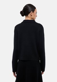 Pull en maille noire avec col, au design court et aux manches longues. Tissu texturé avec une finition lisse, sans matériel visible.
