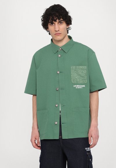 Zelena kratka majica s kratkimi rokavi z gumbskim zapiranjem, dvema sprednjima žepoma in žepom z vzorcem. Vsebuje srebrne gumbe in detajl z logotipom.