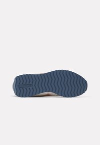 Suela de zapatilla Reebok con un patrón de goma azul, que presenta surcos en zigzag para mayor tracción y el logo "Reebok" estampado en el talón.