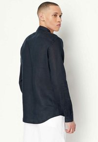 Camicia in lino blu navy con colletto button-down, maniche lunghe e orlo curvo. Presenta una sottile trama e minimi accenti hardware.