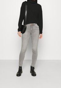 Top de cuello alto negro, jeans ajustados grises y botas negras de tobillo. Las características incluyen un top de ajuste relajado y una silueta elegante en telas suaves.