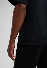 Zwarte t-shirt met korte mouwen van gestructureerde stof, met een relaxte pasvorm en zijsplit-detail, gecombineerd met zwarte broek.