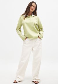 Hellegrünes Langarm-Polohemd mit weißem Kragen, kombiniert mit cremefarbenen, weit geschnittenen Hosen und schlichten schwarzen Sandalen. Glatte Textur, lässiger Schnitt.