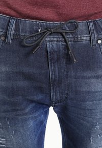 Jeans-joggers i mörkblått med dragsko i midjan, med en lätt sliten struktur och traditionella fickdetaljer.