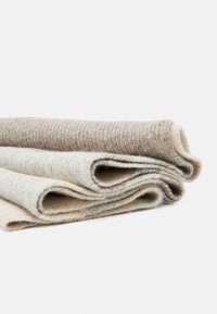 Trois couvertures en laine pliées dans des tons neutres de crème, gris clair et beige. Surface texturée avec des fibres visibles et une finition douce.