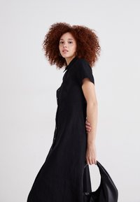 Rochie neagră căptușită, cu mâneci scurte, realizată dintr-un material moale. O textură ușoară, cu o croială ajustată, asociată cu o geantă neagră.