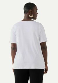 Camiseta blanca de manga corta con un ajuste relajado, que cuenta con un dobladillo trasero recto y aberturas laterales. Textura suave y diseño sencillo.
