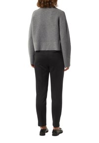 Grau geschnittenen Pullover mit horizontalen Streifen, kombiniert mit schlanken schwarzen Hosen. Die Schuhe bestehen aus schwarzen Loafers mit dekorativen Akzenten.