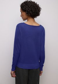 Pull violet en tricot avec manches longues et encolure dégagée. Il présente un ourlet et des poignets côtelés, une texture lisse et une coupe décontractée.