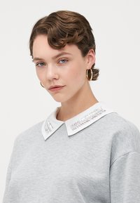 Grauer Sweatshirt mit einem weißen Kragen, der silberne Stickereien aufweist. Das Design ist lässig mit einer bequemen Passform und einem weichen Material.