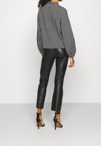 Haut à motif pied-de-cochon noir et blanc avec un col montant, associé à un pantalon en faux cuir noir ajusté et des talons hauts noirs à lanières.