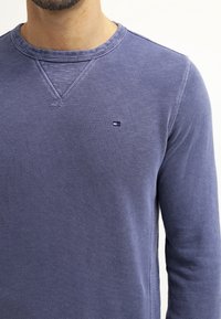 Mikina s dlouhým rukávem a kulatým výstřihem v tmavě modré barvě ze 100% bavlny. Na hrudi se nachází decentní logo značky a texturovaný povrch látky.