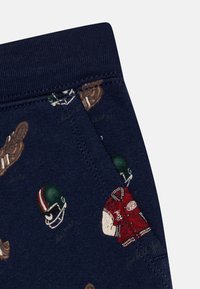 Marinblå bomullstyg med ett upprepat tryck av fotbollshjälmar och en röd varsityjacka. Mjuk textur med ribbad midja.