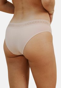 Culotte en coton rose clair avec une délicate bordure en dentelle à la taille. Présente une texture douce, un design taille mi-haute et aucune couture visible.