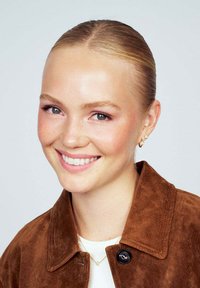 Brun mockajacka med en svart knapp, vit topp och delikat guldsmuck. Slät hud, lätt smink och bakåtkammad frisyr.