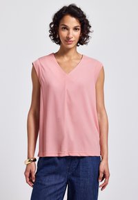 Różowy top z dekoltem w serek i krótkimi rękawami, wykonany z miękkiego materiału. Luźny krój, gładka tekstura, w połączeniu z dżinsowymi spodniami, prezentujący elegancki design.
