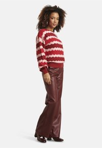 Red and pink wavy-patterned knit sweater with long sleeves, paired with brown faux leather wide-leg pants and matching heels.