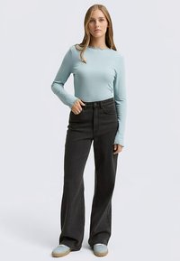 Hellblaues, geripptes Langarmshirt mit Rundhalsausschnitt, kombiniert mit hochgeschnittenen schwarzen Jeans mit weitem Bein und mintgrünen Turnschuhen.