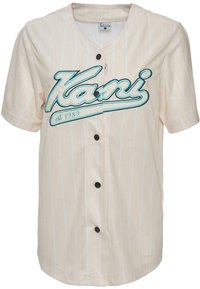 Lys beige kortermet jersey med vertikale striper, med en teal brodert "Kani" logo og fem svarte knapper foran.