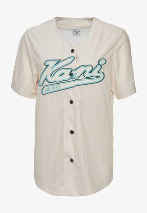 Hele beež lühikeste varrukate ja vertikaalsete triipudega jersesee, millel on türkiissinine brodeuritud "Kani" logo ja viis musta nööpi ees.