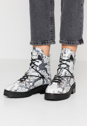 Botas de tobillo con estampado de serpiente en blanco y negro, con una superficie texturizada, ojales de metal y cordones negros, que presentan una suela gruesa negra.