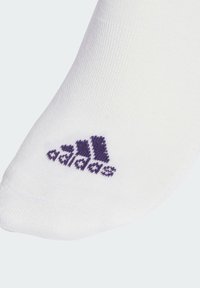 Calcetín blanco hasta el tobillo hecho de una tela texturizada con un logo de Adidas púrpura en el lateral. El diseño es simple y atlético.