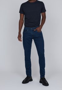 Mörkblå jeans med smal passform, med klassisk femficksdesign och knappstängning, kombinerade med en enkel svart t-shirt och svarta skor.