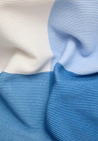 Texturiertes Gewebe mit horizontalen Streifen in verschiedenen Blau- und Weißtönen, mit einer gerippten Struktur und einem auffälligen Farbverlauf.