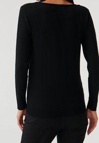 Maglione nero a maniche lunghe in maglia, con scollatura rotonda, corpo aderente e polsini e fondo a coste. Texture liscia e minimalismo nei dettagli.