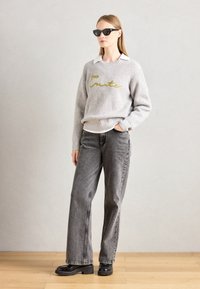 Gray ribbed sweater with yellow embroidered text, paired with high-waisted gray jeans and black chunky shoes, accessorized with black sunglasses.