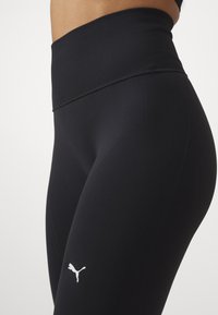 Černé sportovní legíny s ribbovaným vysokým pasem a hladkou texturou, s malým bílým logem na levém stehně.