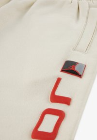 Φόρμες σε κρεμ χρώμα από μαλακό ύφασμα, με κόκκινα γράμματα από καουτσούκ και πάτς λογότυπου σε σκούρο κόκκινο, μαύρο και ασημί.