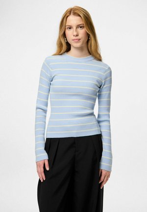 Svijetloplava rebrasta majica s dugim rukavima i žutim vodoravnim prugama, s okruglim izrezom i uskim krojem. Uparena s crnim hlačama.