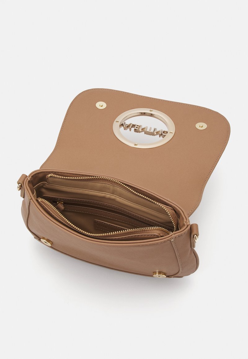 Sac à main en cuir tanné avec un logo circulaire doré découpé sur le rabat, présentant une intérieur zippé et plusieurs compartiments. Accents en métal doré.