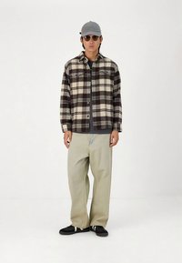 Karirana flanel košulja u crnoj i krem boji, opuštenog kroja svijetle traperice, crne tenisice s bijelim prugama, siva kapa i tamne sunčane naočale.