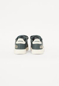 Vihreät synteettisestä nahasta valmistetut tennarit, joissa on valkoinen kuminen pohja ja teksturoitu yksityiskohtaus. Takana on "adidas" ja "STAR WARS" -brändäys.